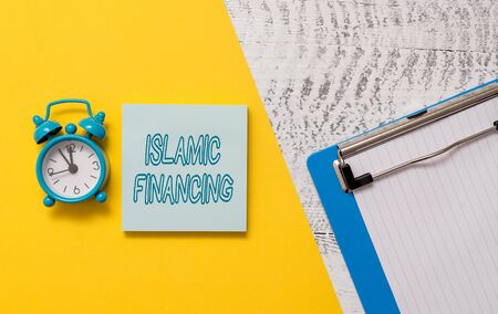 Conceptual hand writing showing Islamic Financing. Concept meaning Banking activity and investment that complies with sharia Notepad colored paper sheet alarm clock wooden backgroundの写真素材