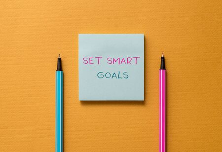 Text sign showing Set Smart Goals. Business photo showcasing giving criteria to guide in the setting of objectives Front view blank colored sticky note two ballpoints cool yolk backgroundの写真素材