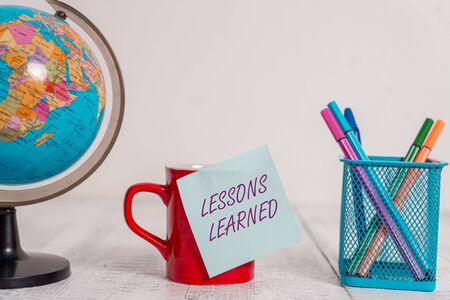 Writing note showing Lessons Learned. Business concept for the knowledge or understanding gained by experience Globe map world earth coffee cup sticky note pens holder wooden tableの写真素材