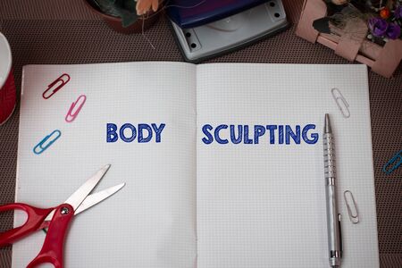 Writing note showing Body Sculpting. Business concept for activity of increasing the body s is visible muscle tone Scissors and writing equipments plus math book above textured backdropの写真素材