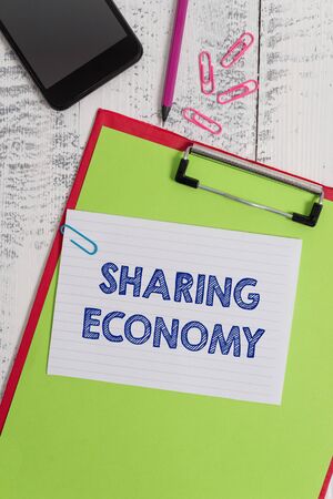 Writing note showing Sharing Economy. Business concept for economic model based on providing access to goods Clipboard sheet pencil smartphone squared note clips wooden backgroundの写真素材