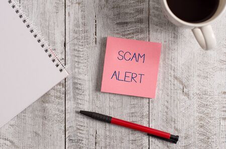Handwriting text Scam Alert. Conceptual photo unsolicited email that claims the prospect of a bargain Stationary placed next to a cup of black coffee above the wooden tableの写真素材