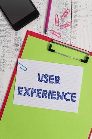 Writing note showing User Experience. Business concept for using website especially in terms how pleasing it is to use Clipboard sheet pencil smartphone squared note clips wooden backgroundの写真素材
