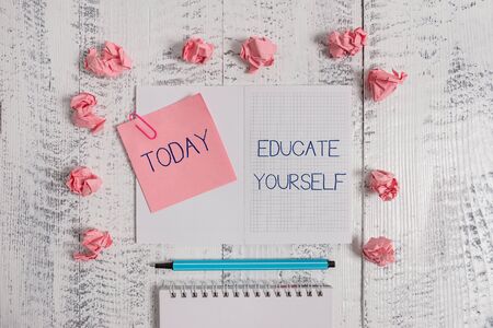 Text sign showing Educate Yourself. Business photo text prepare oneself or someone in a particular area or subject Squared spiral notepad clip note highlighter paper balls wooden backgroundの写真素材