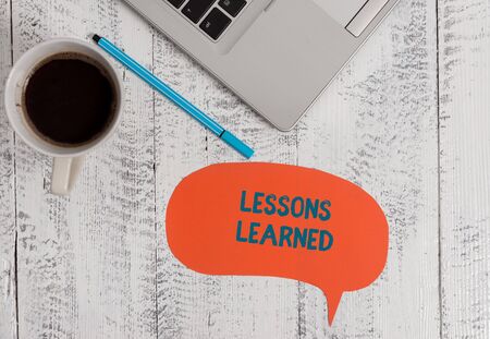 Text sign showing Lessons Learned. Business photo showcasing the knowledge or understanding gained by experience Metallic open laptop speech bubble coffee cup ballpoint pen vintage tableの写真素材