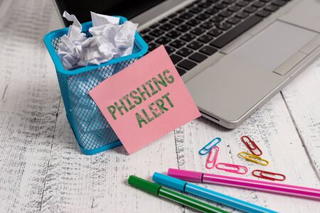 Writing note showing Phishing Alert. Business concept for aware to fraudulent attempt to obtain sensitive information Laptop sticky note waste basket crushed paper clips pens vintage tableの写真素材