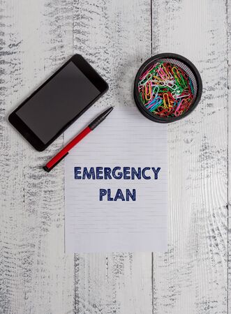 Conceptual hand writing showing Emergency Plan. Concept meaning Procedures for response to major emergencies Be prepared Smartphone paper sheet clips ballpoint wooden vintage backgroundの写真素材