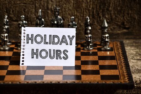 Writing note showing Holiday Hours. Business concept for employee receives twice their normal pay for all hours Empty Notepad Sheet Folded in Half Chessboard Themed Chess Set Piecesの写真素材
