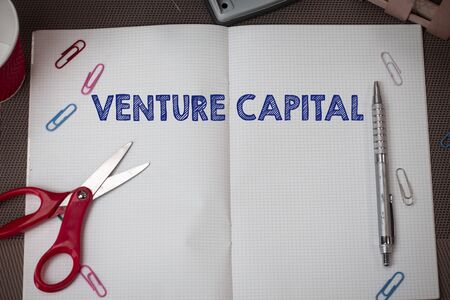 Conceptual hand writing showing Venture Capital. Concept meaning financing provided by firms to small early stage ones Scissors and equipments math book above textured backdropの写真素材