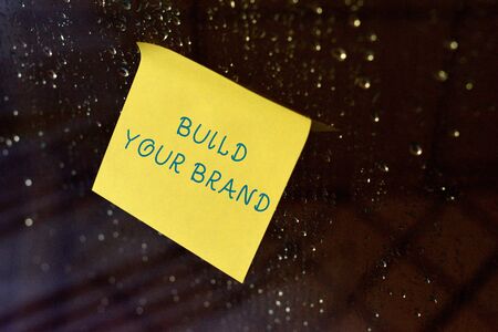 Conceptual hand writing showing Build Your Brand. Concept meaning enhancing brand equity using advertising campaigns Square paper piece notation stick to textured glass windowの写真素材