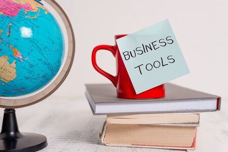 Writing note showing Business Tools. Business concept for Marketing Methodologies Processes and Technologies use Globe map world earth cup blank sticky note stacked books wooden tableの写真素材
