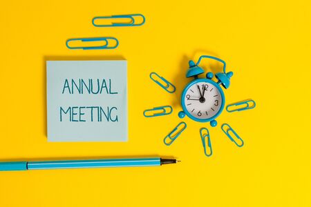 Word writing text Annual Meeting. Business photo showcasing yearly meeting of the general membership of an organization Metal alarm clock wakeup clips ballpoint notepad colored backgroundの写真素材