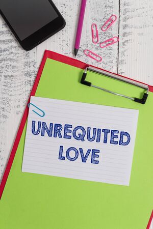 Writing note showing Unrequited Love. Business concept for not openly reciprocated or understood as such by beloved Clipboard sheet pencil smartphone squared note clips wooden backgroundの写真素材