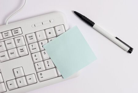 White pc keyboard with empty note paper above white background.の写真素材