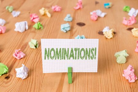 Conceptual hand writing showing Nominations. Concept meaning action of nominating or state being nominated for prize Colored crumpled papers wooden floor background clothespinの写真素材
