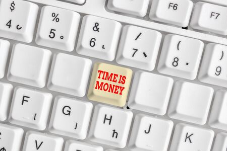 Conceptual hand writing showing Time Is Money. Concept meaning time is a valuable resource Do things as quickly as possible White pc keyboard with note paper above the white backgroundの写真素材