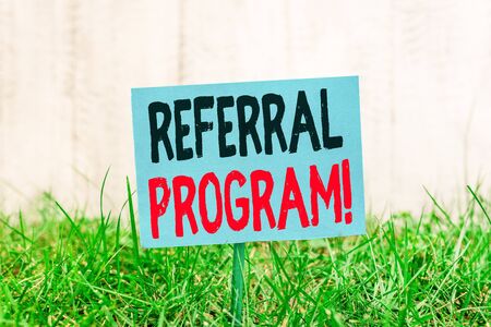 Handwriting text Referral Program. Conceptual photo internal recruitment method employed by organizations Plain empty paper attached to a stick and placed in the green grassy landの写真素材