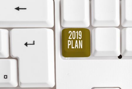 Text sign showing 2019 Plan. Business photo showcasing setting up your goals and plans for the current year or in 2019 White pc keyboard with empty note paper above white background key copy spaceの写真素材