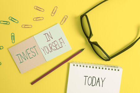 Text sign showing Invest In Yourself. Business photo showcasing learn new things or materials thus making your lot better Square blank sticky notepads pencil clips eyeglasses yolk color backgroundの写真素材