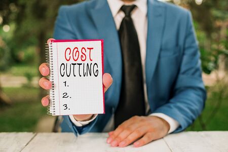 Text sign showing Cost Cutting. Business photo text Measures implemented to reduced expenses and improved profit Man holds empty paper with copy space in front of himの写真素材
