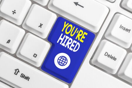 Writing note showing You Re Hired. Business concept for New Job Employed Newbie Enlisted Accepted Recruited White pc keyboard with note paper above the white backgroundの写真素材