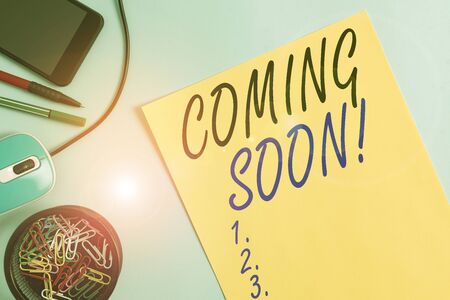 Writing note showing Coming Soon. Business concept for event or action that will happen after really short time Notebook and stationary with gadgets above pastel backdropの写真素材