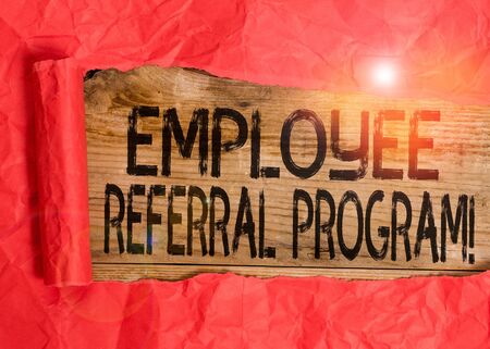 Conceptual hand writing showing Employee Referral Program. Concept meaning employees are rewarded for introducing recruits Cardboard which is torn placed above a wooden classic tableの写真素材