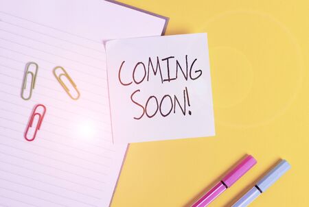 Word writing text Coming Soon. Business photo showcasing event or action that will happen after really short time Empty blue paper with copy space paper clips and pencils on the yellow tableの写真素材