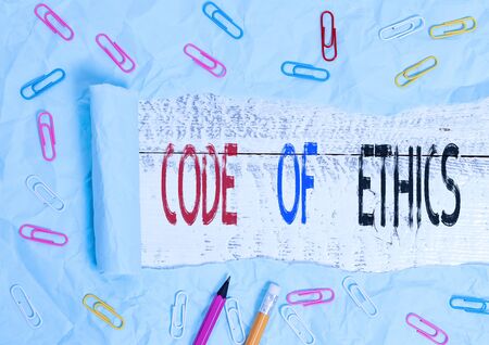 Word writing text Code Of Ethics. Business photo showcasing basic guide for professional conduct and imposes duties Stationary and torn cardboard placed above a wooden classic table backdropの写真素材