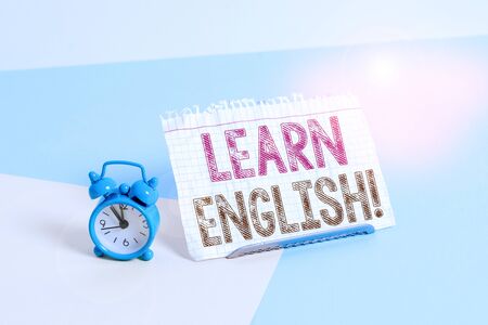 Word writing text Learn English. Business photo showcasing gain acquire knowledge in new language by study Mini size alarm clock beside a Paper sheet placed tilted on pastel backdropの写真素材