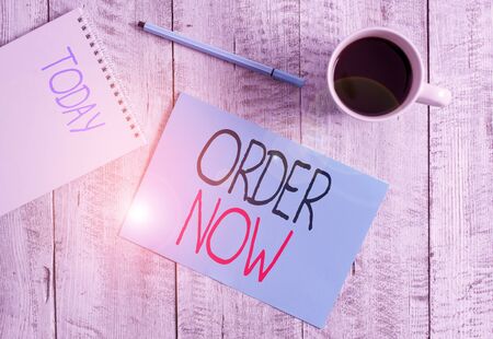 Writing note showing Order Now. Business concept for the activity of asking for goods or services from a company Stationary placed next to a cup of black coffee above the wooden tableの写真素材