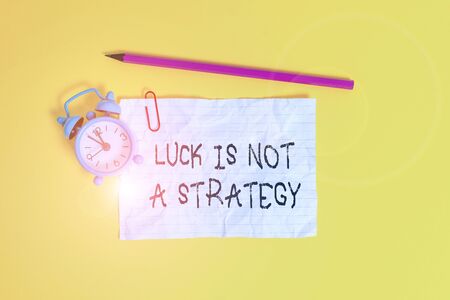 Conceptual hand writing showing Luck Is Not A Strategy. Concept meaning it is not being Lucky when planned intentionally Metal alarm clock ccrushed sheet pencil colored backgroundの写真素材