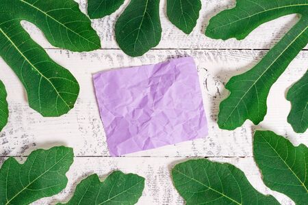 Leaves surrounding notepaper above a classic wooden table as the background