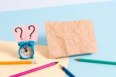 Mini size alarm clock beside stationary placed tilted on pastel backdrop