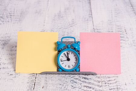 Mini blue alarm clock standing above buffer wire between two notation paper
