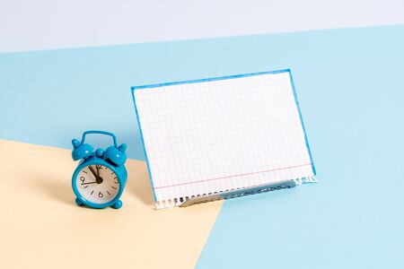 Mini size alarm clock beside a Paper sheet placed tilted on pastel backdrop