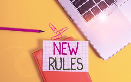 Writing note showing New Rules. Business concept for recently one of a set of explicit or understood regulations Laptop clips pencil paper sheet hard cover notebook colored backgroundの写真素材