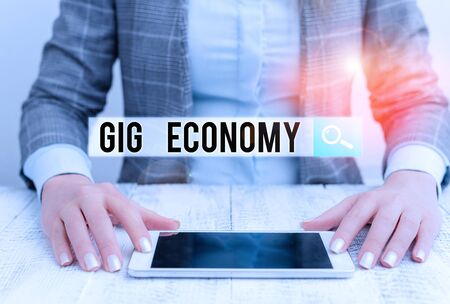 Handwriting text Gig Economy. Conceptual photo free market system in which temporary positions are common Business woman sitting with mobile phone on the tableの写真素材