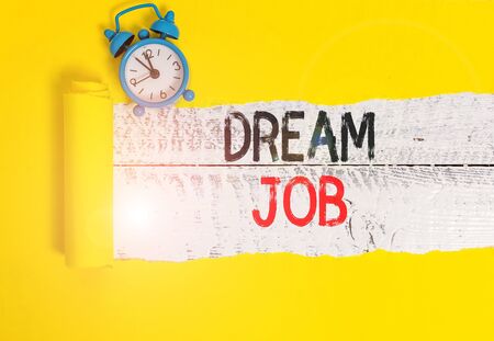 Conceptual hand writing showing Dream Job. Concept meaning An act that is paid of by salary and giving you hapiness Alarm clock and torn cardboard on a wooden classic table backdropの写真素材
