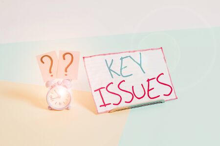 Handwriting text Key Issues. Conceptual photo vital or unsettled matter that showing are arguing about Mini size alarm clock beside a Paper sheet placed tilted on pastel backdropの写真素材