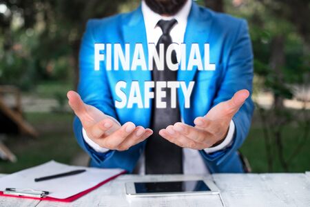 Text sign showing Financial Safety. Business photo showcasing enough money saved to cover emergencies and financial goals Man with opened hands in fron of the table. Mobile phone and notes on the tableの写真素材