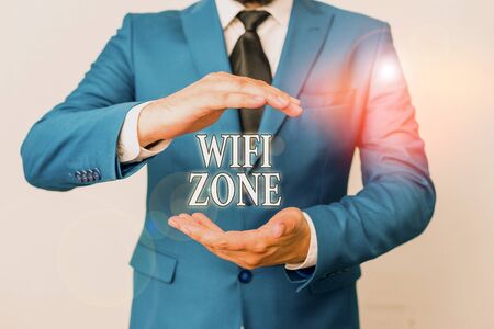 Conceptual hand writing showing Wifi Zone. Concept meaning provide wireless highspeed Internet and network connections Man in front of table. Mobile phone and notes on the tableの写真素材