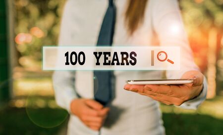 Writing note showing 100 Years. Business concept for Remembering special day for being 100 years in existence Business woman in shirt holding laptop and mobile phoneの写真素材