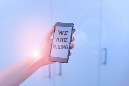 Writing note showing We Are Hiring. Business concept for Workforce Wanted HR recruiting new hire employee Vacancy woman using smartphone and technological devices inside the homeの写真素材