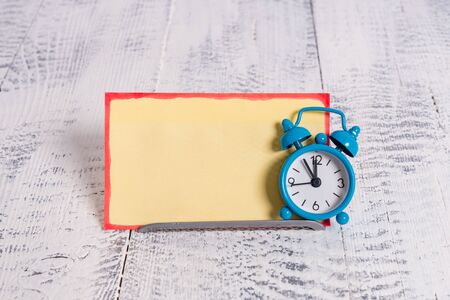Mini blue alarm clock stand tilted above buffer wire in front of notepaper