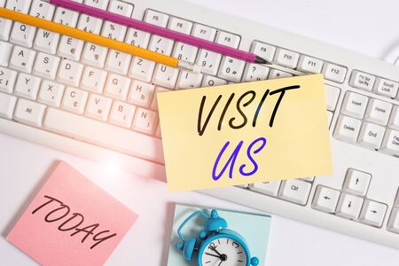Text sign showing Visit Us. Business photo showcasing Invitation Watch A web page Link to Homepage Blog Internet Flat lay above empty note paper on the pc keyboard pencils and clockの写真素材
