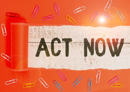 Text sign showing Act Now. Business photo text do not hesitate and start working or doing stuff right away Paper clip and torn cardboard placed above a wooden classic table backdropの写真素材