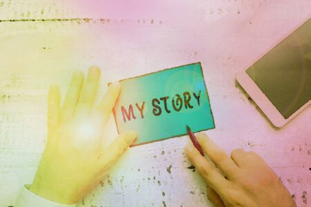Conceptual hand writing showing My Story. Concept meaning the things or situations that have happened to someone in life Hand hold note paper near writing equipment and smartphoneの写真素材