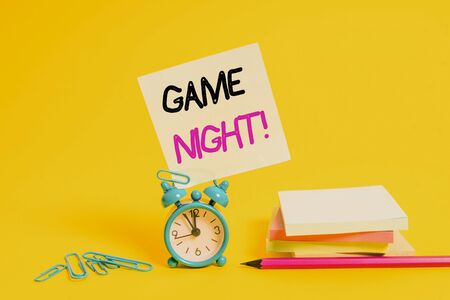 Conceptual hand writing showing Game Night. Concept meaning usually its called on adult play dates like poker with friends Alarm clock pencil clips note stacked notepads colored backgroundの写真素材