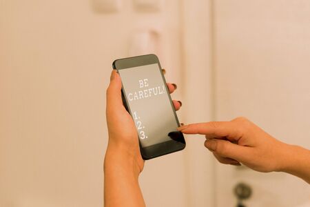 Handwriting text Be Careful. Conceptual photo making sure of avoiding potential danger mishap or harm woman using smartphone office supplies technological devices inside homeの写真素材